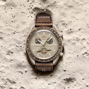 Beige chronograph men's watch with brown strap displayed on a textured, moon-like surface